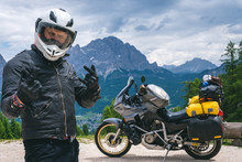 Close Up Portrait Of Happy Biker Man In Helmet And Stylish Leather Jacket. Adventure Touring Motorcycle On Background, High Top Mountains, Tourism Travel Concept, Copy Space. Dolomites