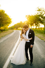 Joyful young couple is hugging on the road at sunset.