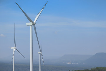 Wind turbine for electricity generation Behind the mountains in the sky there are white clouds on a sunny and foggy day.