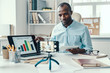 © gstockstudio - Intelligent young African man in shirt showing chart while making social media video
