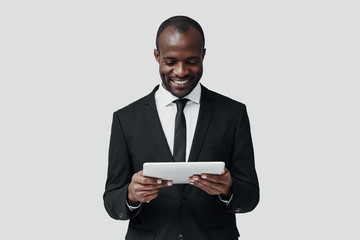 Sticker - Charming young African man in formalwear working using digital tablet while standing against grey background