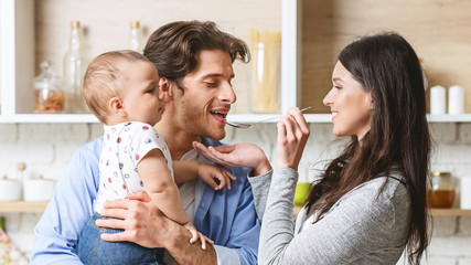 Wall Mural - Cheerful woman feeding her millennial husband with baby