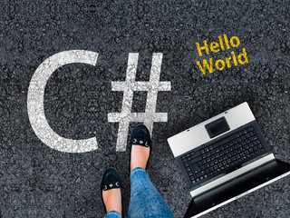 c sharp programming language. woman legs in shoes standing next to laptop and c sharp, c# on asphalt