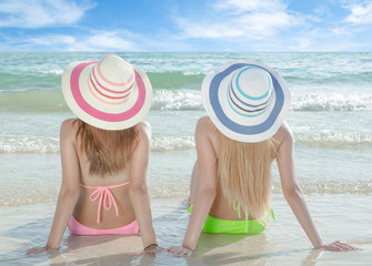 Two young women sitting by the beach in summer.