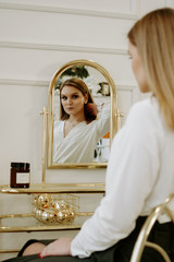 Wall Mural - Beautiful woman in a strict white blouse in her room near her dressing table