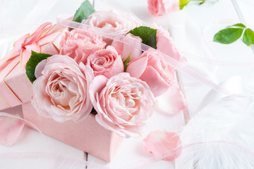 Beautiful pink flowers in gift box with ribbons closeup on white wooden table.