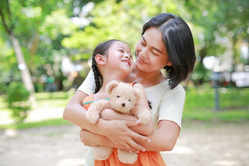 Portrait of happy Asian mother cuddle daughter and hugging teddy bear doll in the garden. Mom and child girl with love and relationship concept.