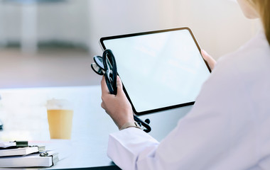 Wall Mural - closeup shot of doctor holding stethoscope and using tablet while sitting at table, blank screen for