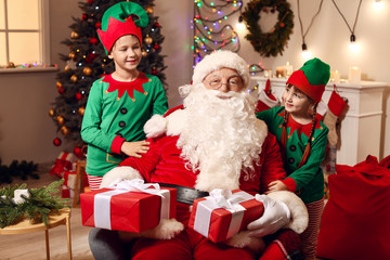 Wall Mural - Santa Claus and little elf kids with gifts in room decorated for Christmas