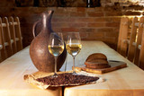 Fototapeta Sawanna - Two glasses of white wine, grape seeds, a clay jug and a few pieces of bread on a wooden table in a restaurant