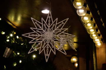 Wall Mural - Golden christmas tree. Glittering star shaped Christmas ornament on blurry background of Christmas lights in darkness. Silver ornate star closeup. New Year decor and row of retro glass bulbs 