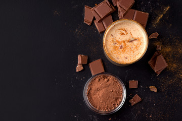 lassi chocolate cold indian drink on a black background next to cocoa and chocolate. top view with copy space