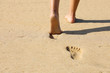 Beach woman legs feet walking barefoot on sand leaving footprints on golden sand in sunset. Vacation travel freedom people relaxing in summer.