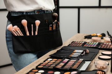 Professional makeup artist with belt organizer near wooden table indoors, closeup