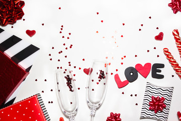 Wall Mural - Valentine's day romantic party concept. Gift boxes, heart shape, confetti, glasses of champagne, sweets, black and red decorations on white background. Top view, flat lay, copy space