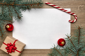 Christmas or New Year composition. White sheet of paper with copy space, gift box, candy cane, Christmas ball and Christmas tree branches on wooden background. Flat lay, view from above