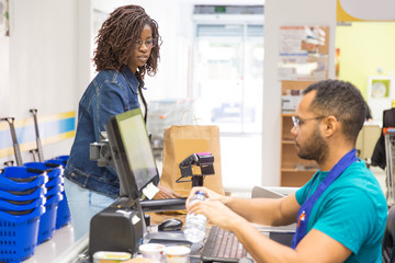 Wall Mural - Side view of male cashier scanning goods at checkout. Young woman with buying groceries in supermarket. Shopping concept