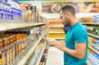 © Mangostar - Focused African American man holding alcohol drink. Serious bearded guy standing in aisle and looking at bottle. Shopping concept