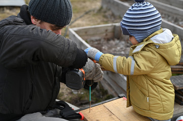 a father and a young son together make a construction, bed for plants, of wooden boards with a screwdriver. family hobby 