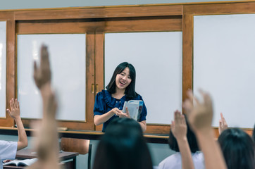 Wall Mural - An smiling Asian female high school teacher teaches the white uniform students in the classroom by asking questions and then the students raise their hands for answers.