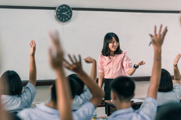 Wall Mural - An smiling Asian female high school teacher teaches the white uniform students in the classroom by asking questions and then the students raise their hands for answers.