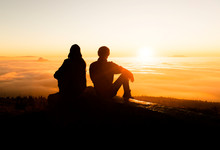Silhouette Of Two Friends Man Standing On A Rock At Sunrise On The Fog Of Success And Serenity.