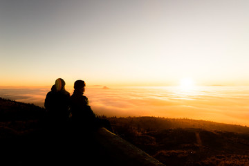 Silhouette of two friends man standing on a rock at sunrise on the fog of success and serenity.