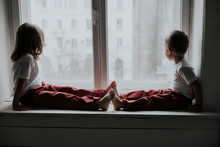 Boy And Girl Sitting On The Windowsill Looking Out The Window