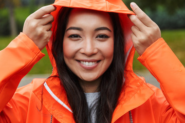 Sticker - Smiling young asian woman wearing raincoat walking outdoors