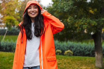 Wall Mural - Smiling young asian woman wearing raincoat walking outdoors