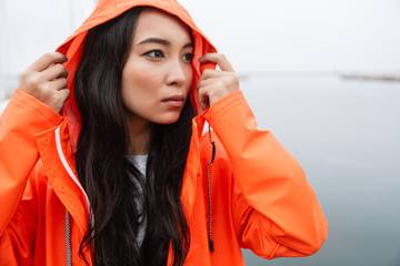 Sticker - Attractive young asian woman wearing raincoat walking outdoors