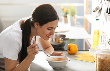 Sticker - Young woman eating tasty vegetable soup at countertop in kitchen