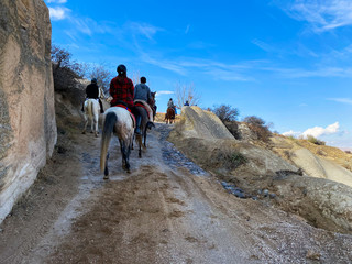 Wall Mural - Tourists on horseback go along the road through the mountains. Tourist route. Cappadocia Valley. Turkey. November 5, 2019.