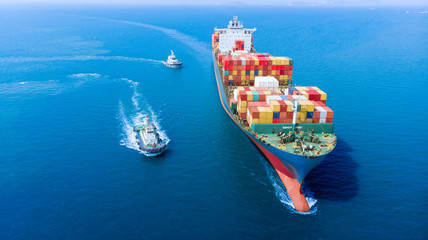 Aerial of cargo ship carrying container with tugboat working near and running for export  goods  from  cargo yard port to custom ocean concept freight shipping by ship .