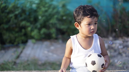 Wall Mural - Asian kid 2 year old from Thailand sitting on the garden alone. He using a safety cycling protection equipment concept. and he looking the wood on his hands.                              