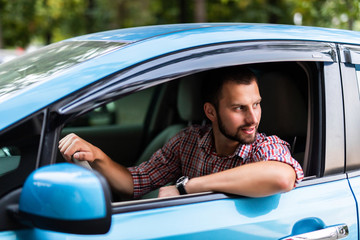 Electric car driver - green energy biofuel concept. Male behind wheel. Man driving new ecofriendly vehicle in nature forest. Young male owner proud confident looking at camera,