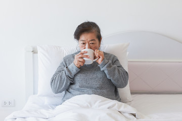 Wall Mural - Asian senior old woman drinking coffee or tea on the bed