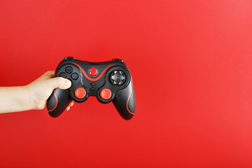 Wall Mural - A child's hand holds a gamepad on a red background. Free space, minimalistic creative concept of the Younger generation of gamers.