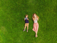 Mom And Son Are Lying On The Grass In The Park. Mom Looks At The Phone, Son Looks At The Tablet. Photos From The Drone, Quadracopter