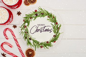 Wall Mural - top view of candy canes, two cups of cocoa and christmas pie with Merry Christmas illustration on white wooden table