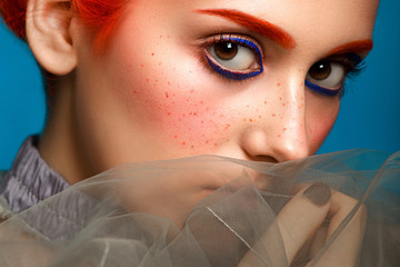 Beautiful girl with colored in red hair and blue eyeliner makeup isolated on blue background