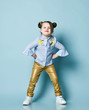 Playful frolic kid girl in blue shirt and gold leather pants is cool posing with her hands on her hips and chin thrust