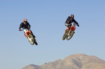 motocross racers performing stunt in midair against blue sky