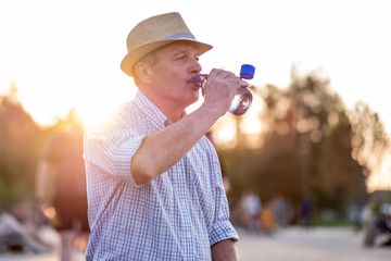 Senior man drinking bottled water standing outdoor on summer evening