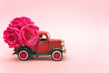 Red toy truck delivering bouquet of rose flowers on pink background. February 14, Valentine's day, 8 March, International Women's Day. Flower delivery. Copy space