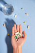 © Maki Company Limited/Stocksy - Human hands holding pills and glass of water on blue