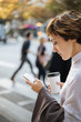 © Pietro Karras/Stocksy - Human using smartphone with cup of drink on street