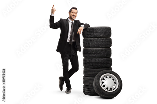 Fotografía Young businessman pointing above and leaning on a pile of car tires