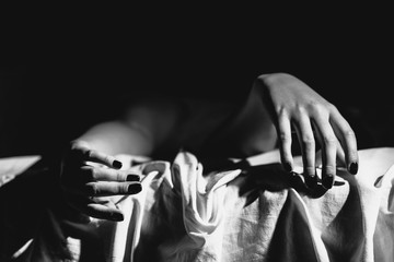 Close up on female young woman's girl's beautiful hands woman lying on the bed black and white nail polish in dark room crossed fingers on sheet gentle passion love temptation emotion concept