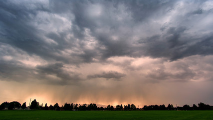 Wall Mural - Storm clouds rolling over the landscape  looking through green grassy field in Utah.